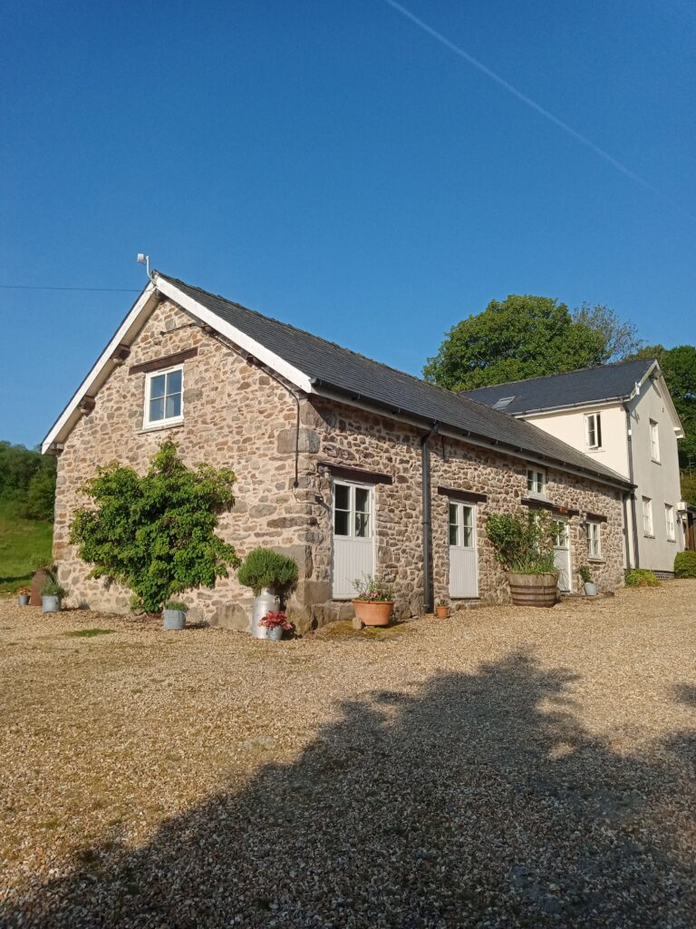 The converted stone barn at Graig Fawr, with its slate roof and white doors, under a clear summer sky