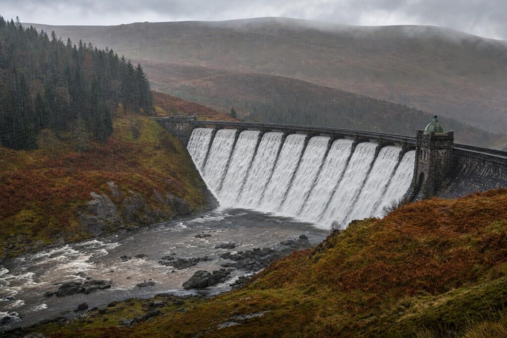 A Victorian stone reservoir dam in the Mid Wales hills overflowing in heavy autumn rain.